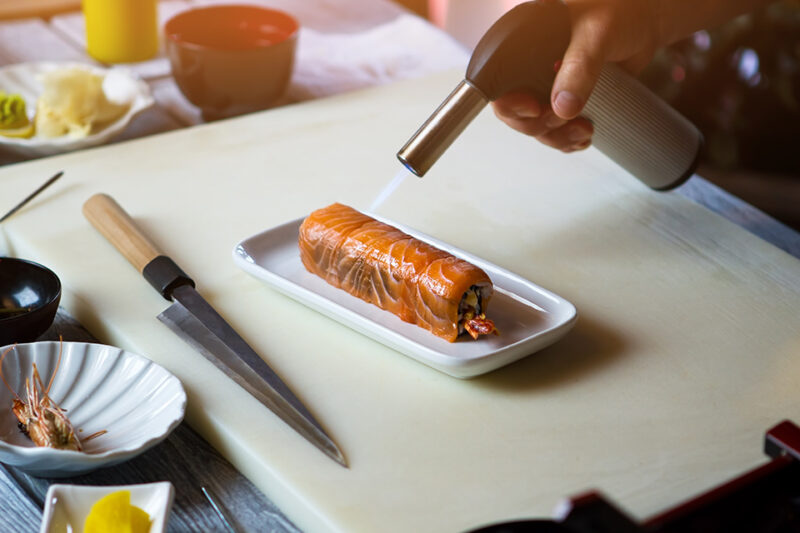 Hombre utilizando una antorcha de cocina para cocinar sushi
